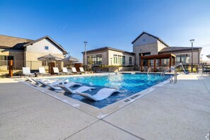 A swimming pool with lounge chairs and a covered area, surrounded by buildings with large windows and a clear sky. - Near Lake Texoma 1BR-Kingbed I Pool-GYM (Sherman)