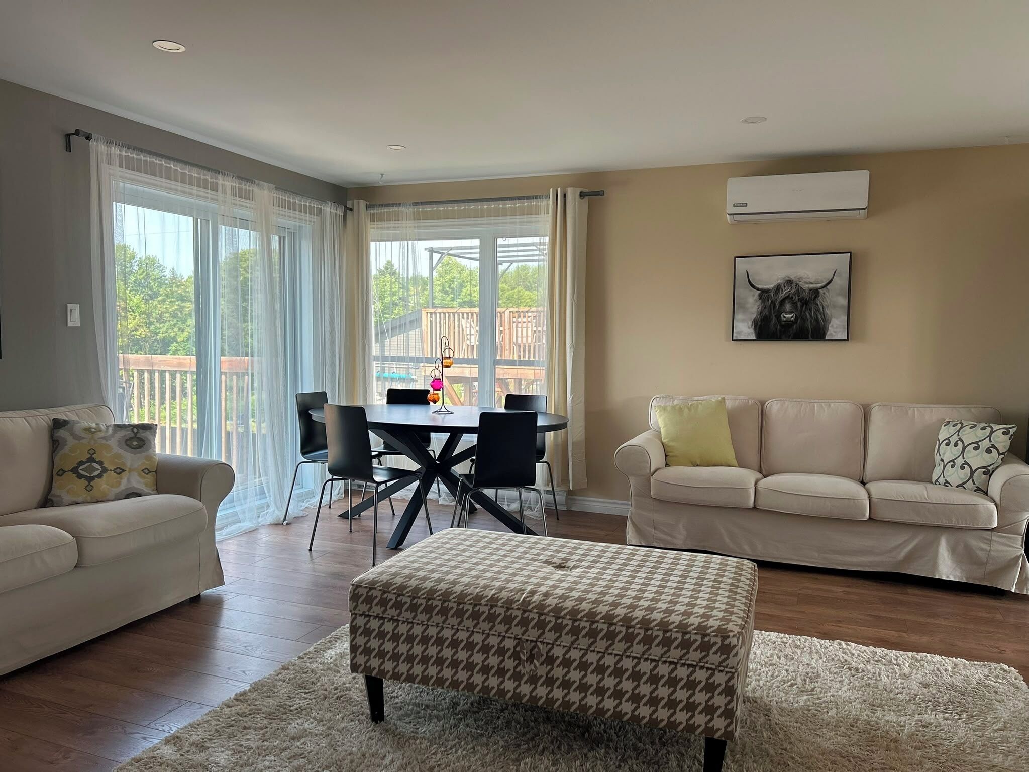 A living room with a sofa, ottoman, dining table, chairs, and a large window with curtains.
