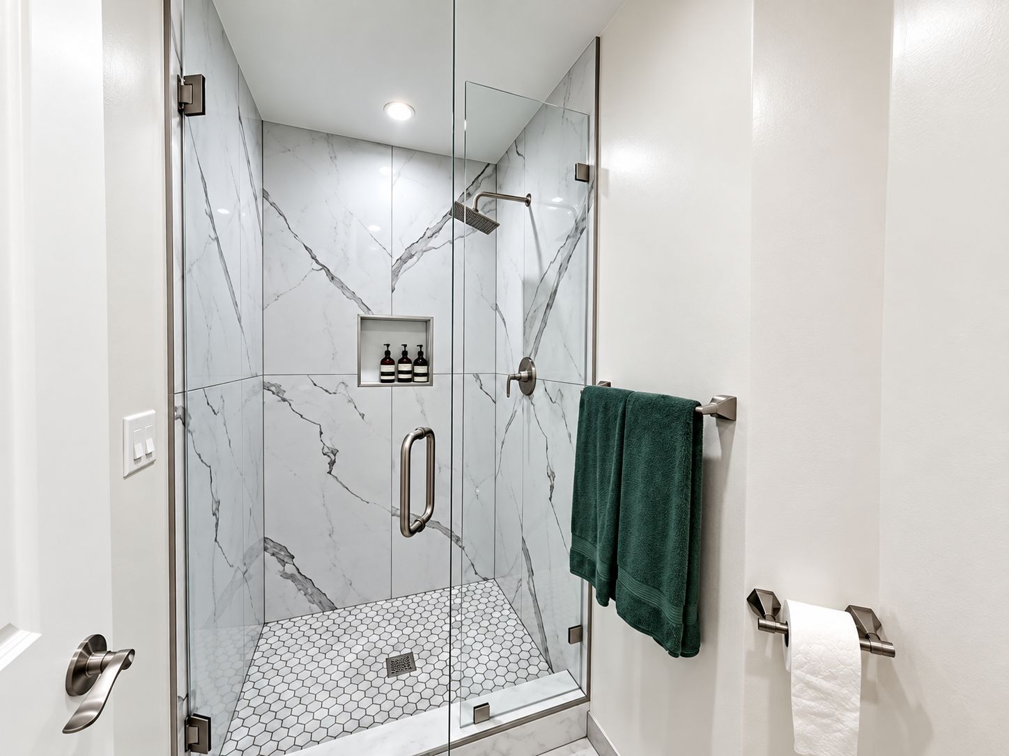 A modern shower with glass doors, a marble wall, and a green towel.
