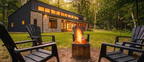 A modern house with a fire pit and two Adirondack chairs in the yard.
