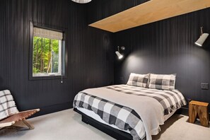 Ein Schlafzimmer mit einem Bett, einem Fenster, einem Nachttisch und einer Lampe.
