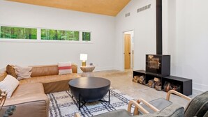 A modern living room with a sofa, a coffee table, a fireplace, and a view of the outdoors.