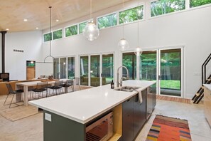 Una cocina moderna con una isla grande, un comedor con mesa larga y vistas a un bosque a través de amplios ventanales.