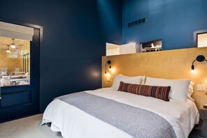 Un dormitorio con cama, lámparas de noche, cabecero de madera y ventana con vista a un comedor.