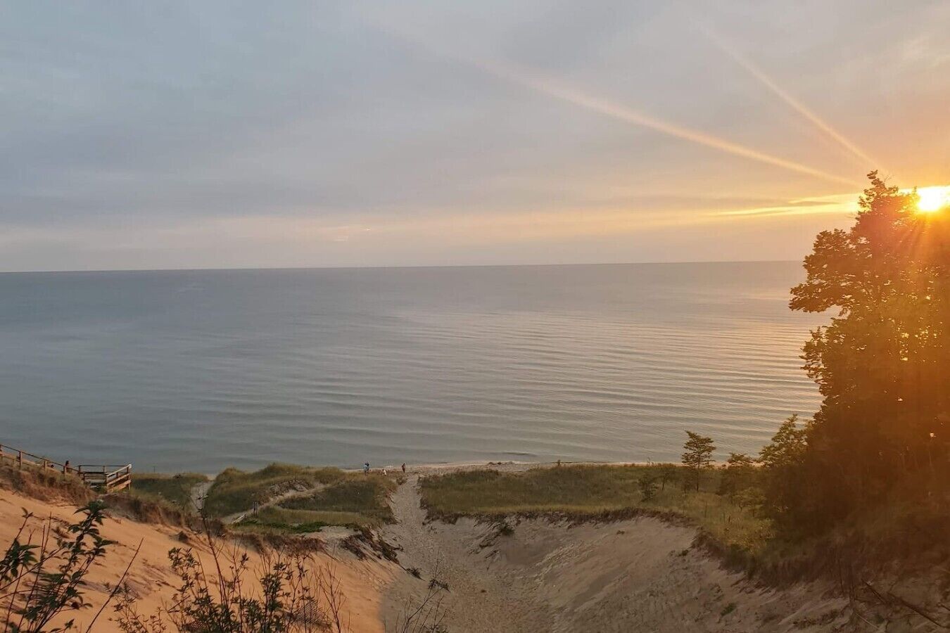 Un paisaje costero con vista despejada al mar, un sendero de arena y una línea de árboles.