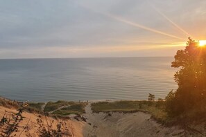 A coastal landscape with a clear view of the sea, a sandy path, and a tree line.