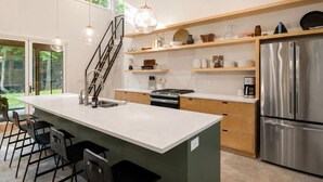 Una cocina moderna con una isla grande, electrodomésticos de acero inoxidable y una escalera que lleva a un nivel superior.