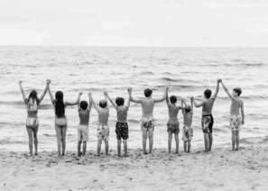 A group of people standing on a beach facing the ocean.