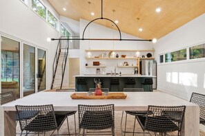 A modern kitchen with a central island, black wire mesh chairs, and a wooden dining table. - Secluded Modern Cabin with Hot tub / Firepit / 2mins to Beach (Holland)