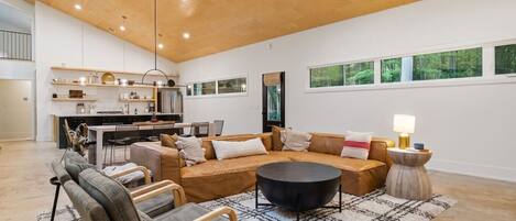 A modern living room with a sofa, chairs, a coffee table, and a kitchen in the background.