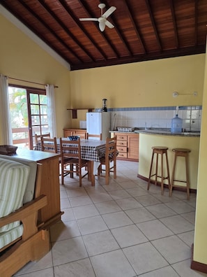 A kitchen with a dining area, a ceiling fan, and a window with curtains. - Charming 2-Bedroom Apartment in Enchanting Porto Seguro with AC Comfort (Porto Seguro)