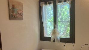 Un letto singolo con materasso bianco e cuscino a forma di personaggio dei cartoni animati, un comodino con una lampada e una finestra con tende leggere.