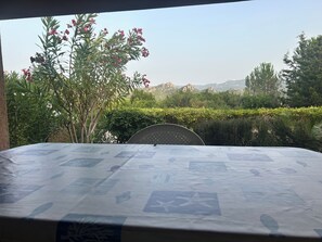 A table with a patterned tablecloth, a chair, and a view of a garden with various plants and a distant mountain range. - Adorable 2-bedroom house with AC in Costa Paradiso (Trinita d'Agultu and Vignola)