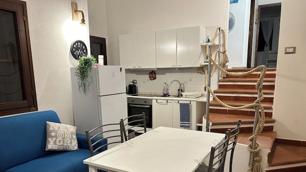 Un ambiente abitativo compatto con angolo cottura, zona pranzo e scala.