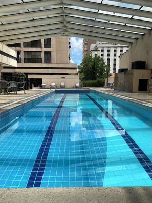 A swimming pool with clear blue tiles, surrounded by lounge chairs and a covered area. - Functional apartment opposite Congonhas Airport. (São Paulo)