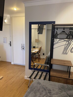 A compact room with a bed, a small table, a mirror, a TV mounted on the wall, and a door leading to another room. - Functional apartment opposite Congonhas Airport. (São Paulo)