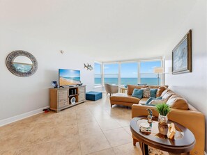 Ein Wohnzimmer mit Blick auf den Ozean, einem runden Spiegel, einem Sofa, einem Couchtisch und einem Beistelltisch mit Pflanze.