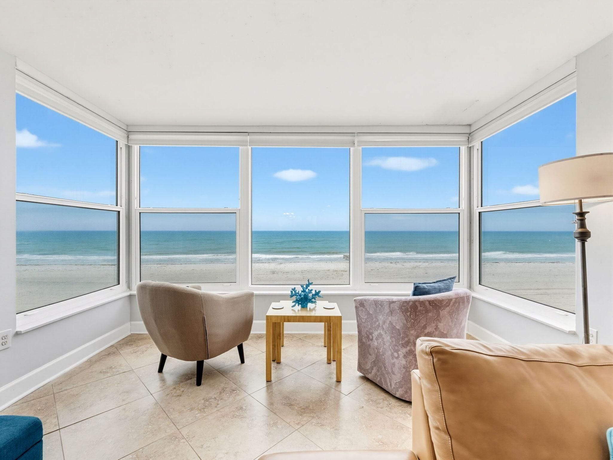 Une chambre avec vue sur la plage, deux fauteuils, une petite table et une lampe.