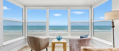 Una habitación con vista a la playa, dos sillones, una mesita y una lámpara.