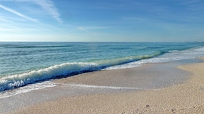 Ein Strand mit sanft anschwellenden Wellen, blauem Himmel und Land in der Ferne.