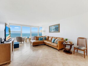 Ein Wohnzimmer mit großem Fenster mit Meerblick, ein braunes Ledersofa, ein Holztisch und ein gerahmtes Gemälde an der Wand.