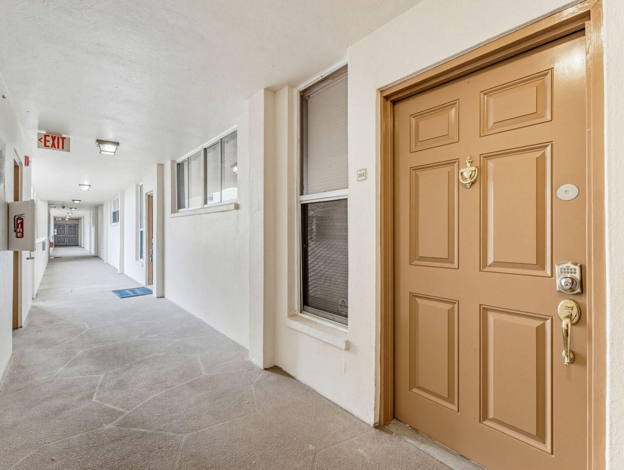 A hallway with a fire alarm, exit sign, and a door with a keypad lock.
