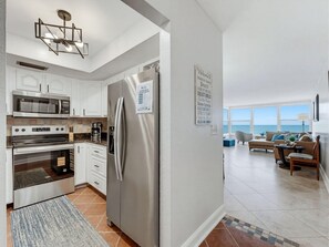 A modern kitchen with stainless steel appliances, a dining area with a view of the ocean, and a living room with a large window. - Madeira Vista 202 (Madeira Beach)