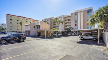 A parking area with multiple cars, a covered parking structure, and a building with multiple floors and balconies.