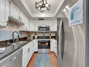 A modern kitchen with white cabinets, stainless steel appliances, and a black countertop. - Madeira Vista 202 (Madeira Beach)