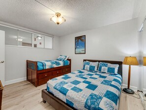 A bedroom with a large bed, a nightstand, a dresser, a window, and a ceiling light fixture. - Madeira Vista 202 (Madeira Beach)