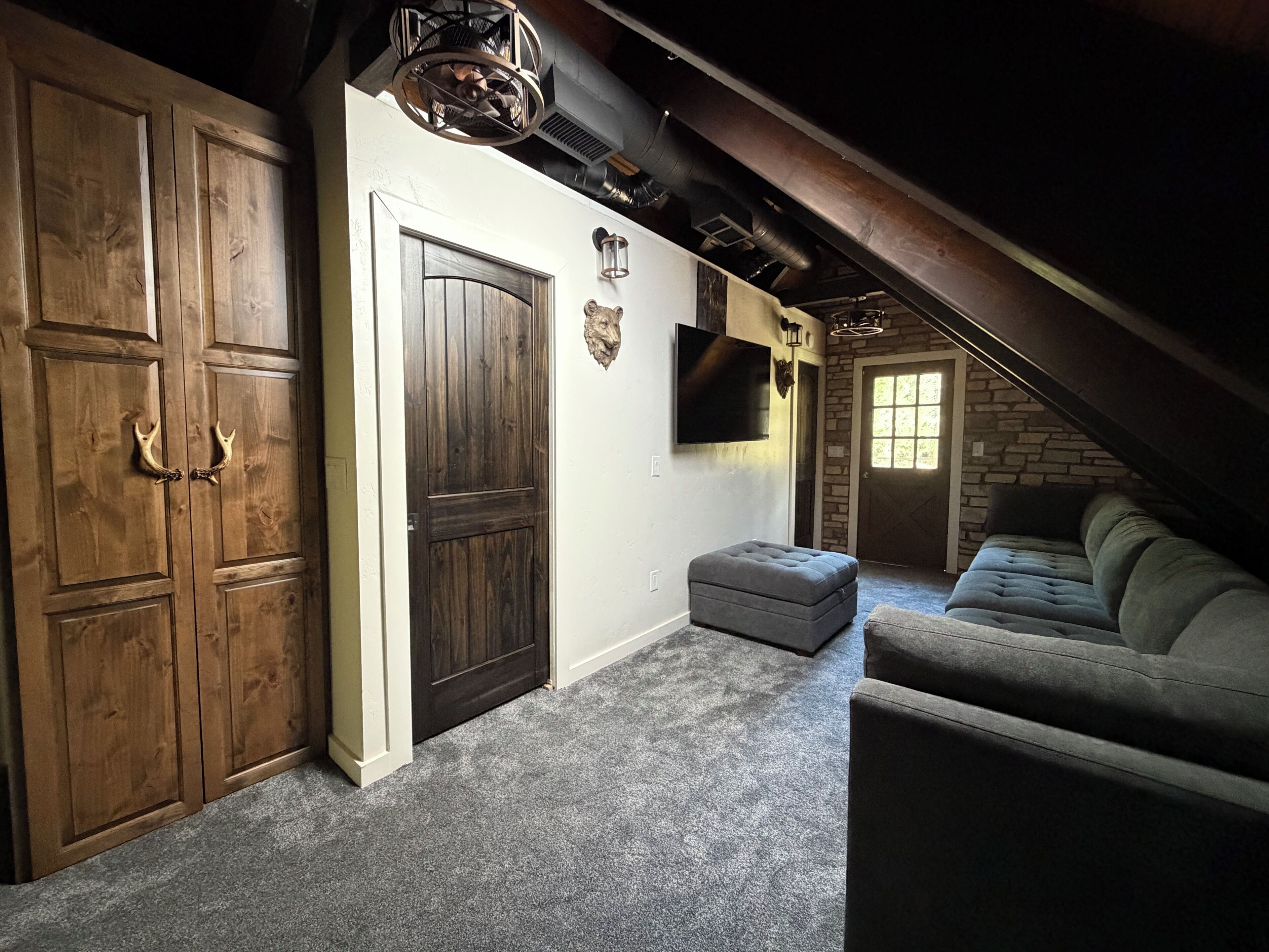 Et værelse med hvælvet loft, en stor trædør, en grå sofa og en stenvæg.