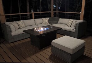 A deck with a sectional sofa, a glass-top coffee table with a fire feature, and a cushioned ottoman. - Fantastic 5-bedroom cabin in North Fork perfect for relaxing getaways (North Fork)