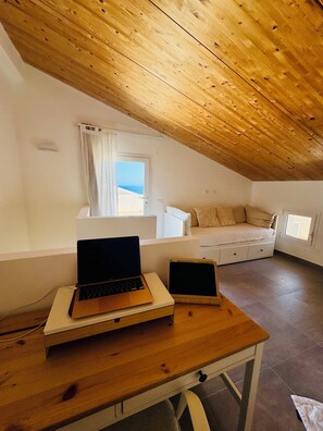 A cozy attic room with a sloped ceiling, a bed, a window with a view, and two laptops on a table. - Largest 2 Bedroom Oceanview Rooftop Apartment in Borto 84 (Sicilia)