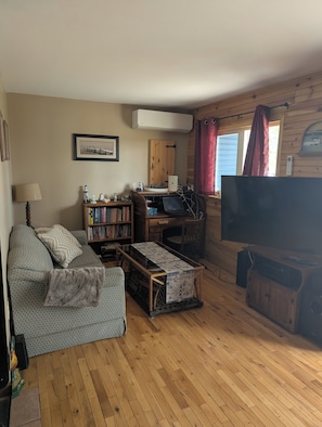 A cozy living room with a sofa, a coffee table, a bookshelf, a desk with a computer, and a television.