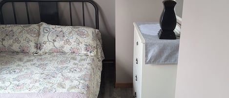 Une chambre à coucher avec un lit, une table de chevet avec une lampe, un tableau encadré au mur et une commode.