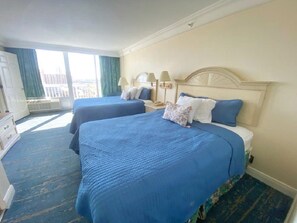 Ein Hotelzimmer mit zwei Betten, einem Nachttisch, einer Lampe und Blick auf die Stadt.