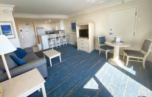 Una habitación con sofá, una mesita, televisor, kitchenette y una puerta.