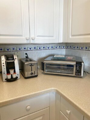 Una cocina con armarios blancos, cafetera, tostadora y horno tostador.