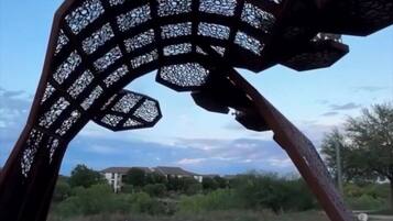 Una escultura de metal con un diseño de celosía, ubicada sobre una plataforma de concreto con escalones que la rodean.