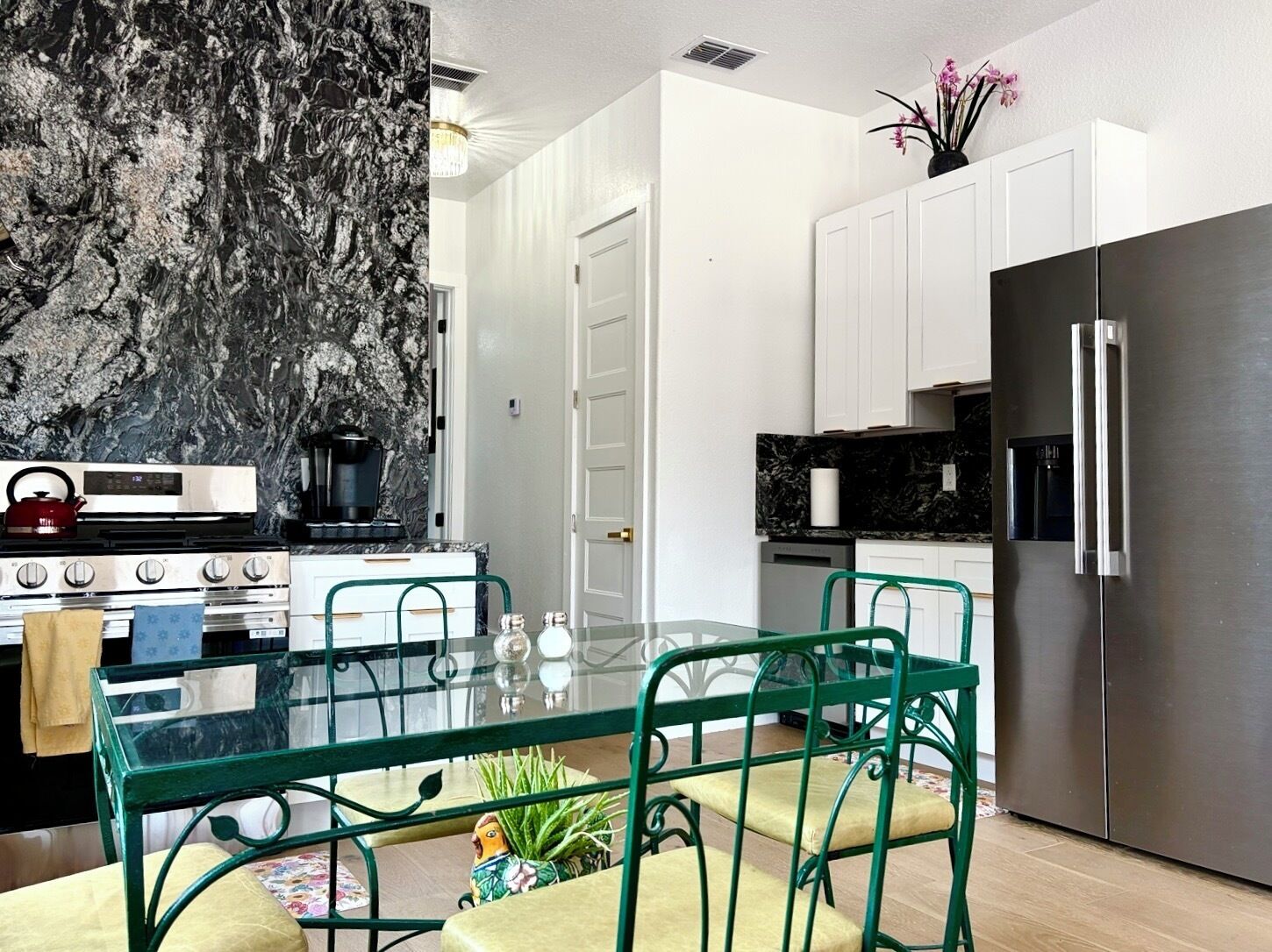 Una cocina moderna con protector de encimera de mármol, electrodomésticos de acero inoxidable y una mesa de comedor de vidrio con sillas verdes.