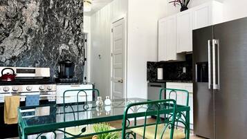 Una cocina moderna con protector de encimera de mármol, electrodomésticos de acero inoxidable y una mesa de comedor de vidrio con sillas verdes.