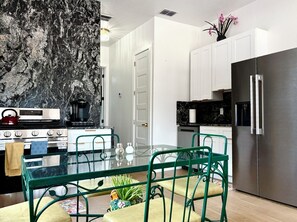 Una cocina moderna con protector de encimera de mármol, electrodomésticos de acero inoxidable y una mesa de comedor de vidrio con sillas verdes.