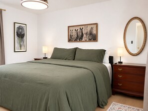 A bedroom with a bed, two bedside tables, a dresser, a mirror, and two wall-mounted lamps.