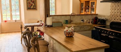 A kitchen with a central island, wooden chairs, a chandelier, and a large window.