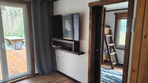 Habitación con televisión de pantalla plana en la pared, piso de madera, puerta corrediza de vidrio que da a un espacio exterior y una escalera en la esquina.