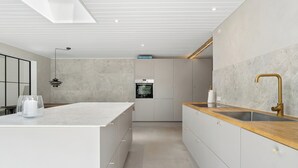 A modern kitchen with a central island, a built-in oven, and a wooden countertop with a gold faucet. - Luxury retreat surrounded by nature (Rønde)