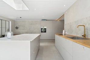 Eine moderne Küche mit einer zentralen Kochinsel, einem eingebauten Backofen und einer Holzausziehtheke mit goldenem Wasserhahn.