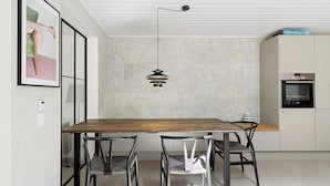 A modern kitchen with a wooden dining table, two chairs, a pendant light, and a built-in oven. - Luxury retreat surrounded by nature (Rønde)