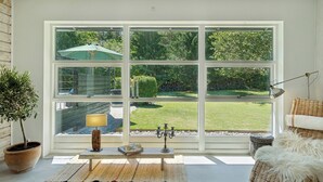 A room with a large window, a potted plant, a lamp, and a wicker chair. - Luxury retreat surrounded by nature (Rønde)