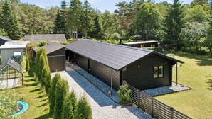 A wooden cabin with a gravel driveway, surrounded by trees and a fenced yard. - Luxury retreat surrounded by nature (Rønde)